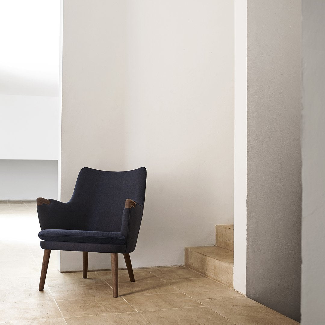 Navy blue upholstered armchair with wood accents, set against a neutral background and textured stone flooring.