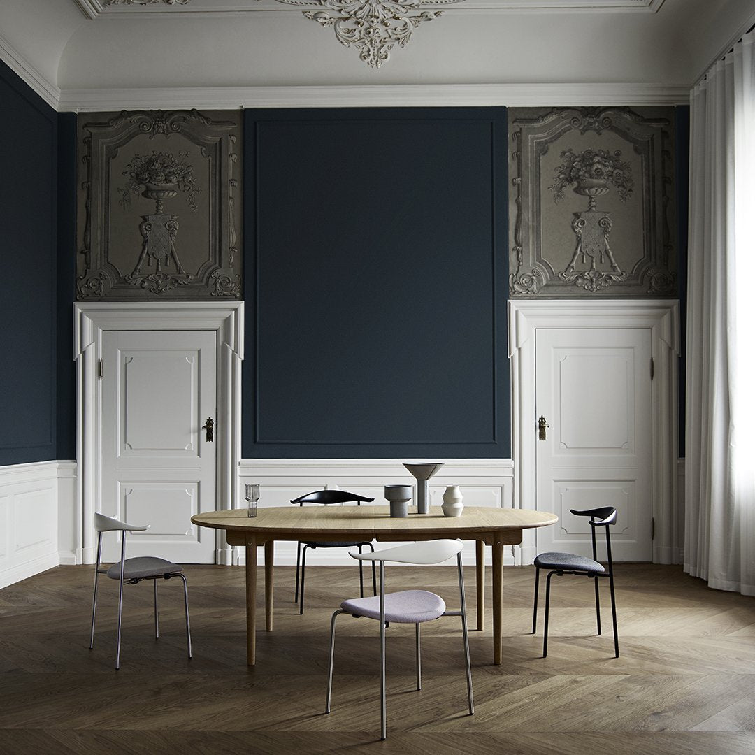 Modern dining room with deep navy blue walls and a light wood table, featuring black and gray accent chairs.