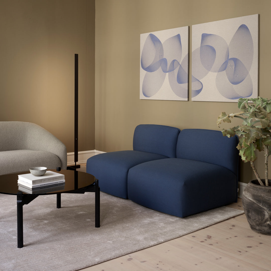 Navy blue modular sofa with smooth, modern lines, set against a neutral-toned wall and abstract art pieces in soft hues.