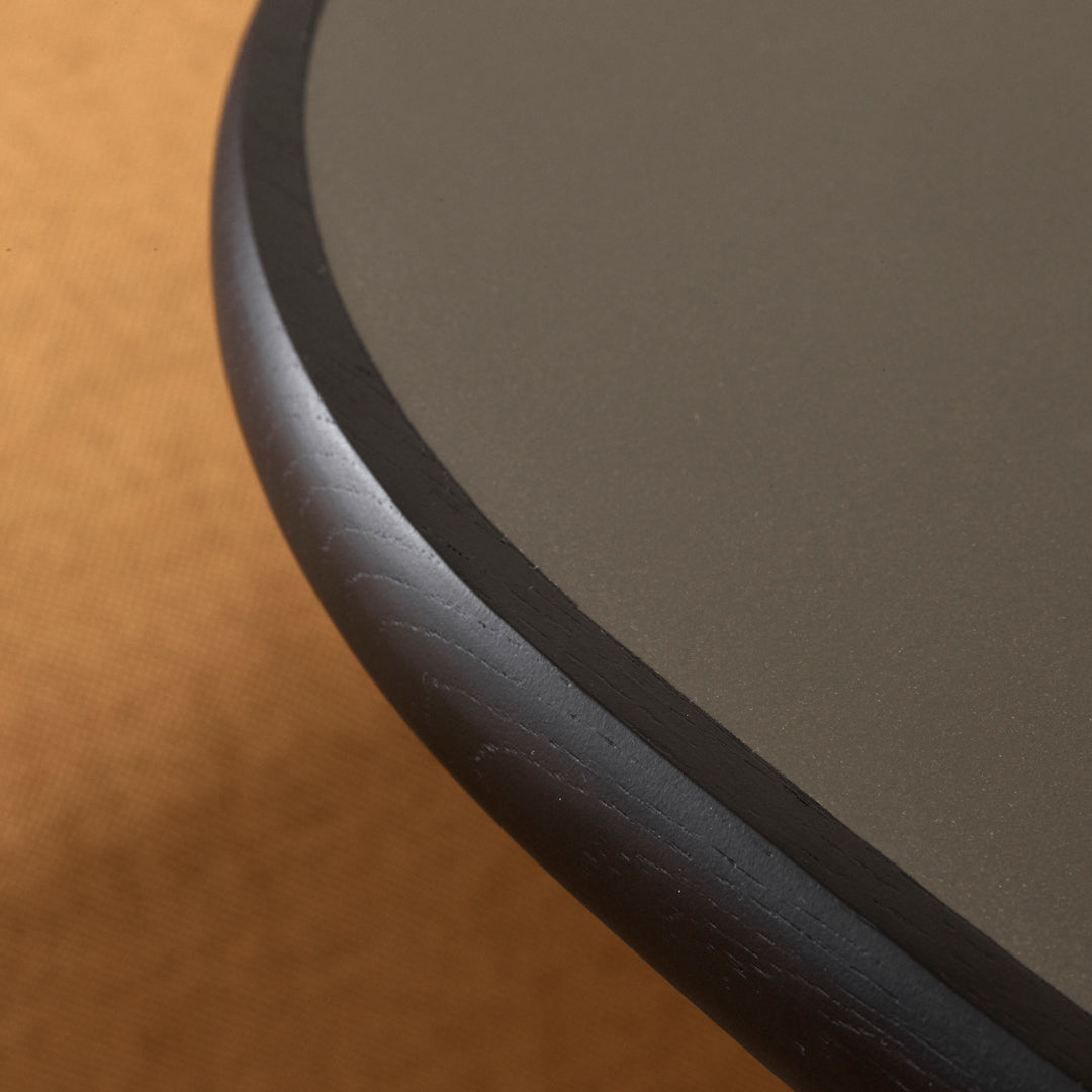 Close-up of a dark gray table edge with a sleek black trim, set against a warm tan background.