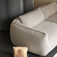Soft beige couch with textured fabric against a dark backdrop and vertical gray panel, complemented by a natural wood accent.