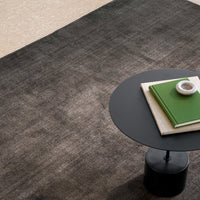 Textured dark gray area rug with subtle patterns, complementing a minimalist black table and green accents.