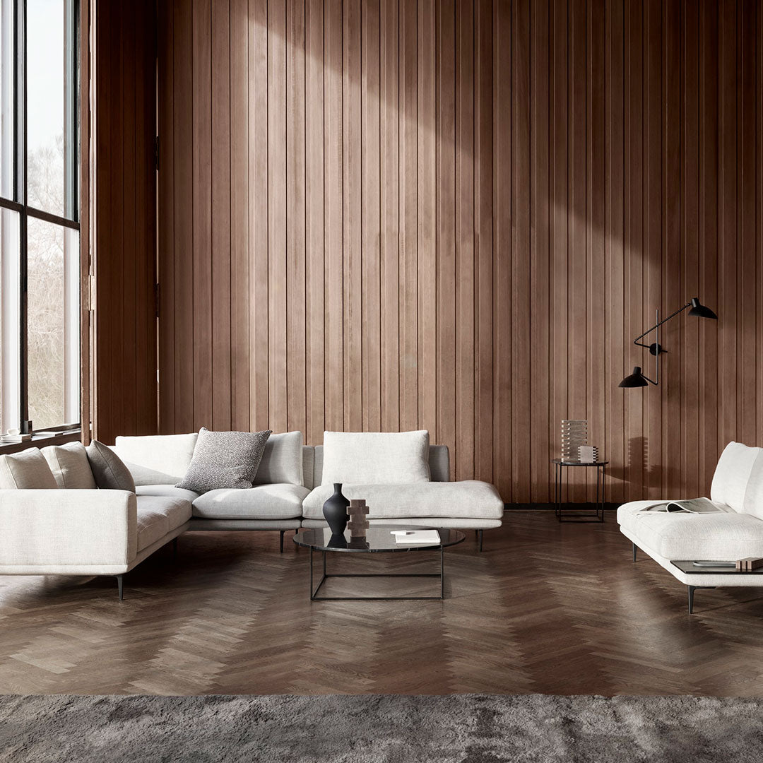Modern white sectional sofa with neutral accent pillows, set against a rich wood-paneled wall and herringbone-patterned floor.