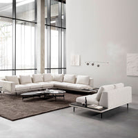 Modern white sectional sofa on a dark brown rug, featuring clean lines and minimalist design in a bright, spacious setting.
