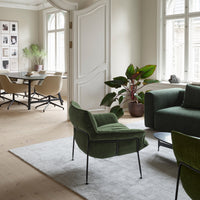 "Green upholstered chair with black metal legs, paired with a grey rug and light beige decor in a modern interior."