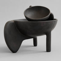 Black matte ceramic bowls with smooth, rounded edges and unique organic shapes, stacked atop a sculptural base.