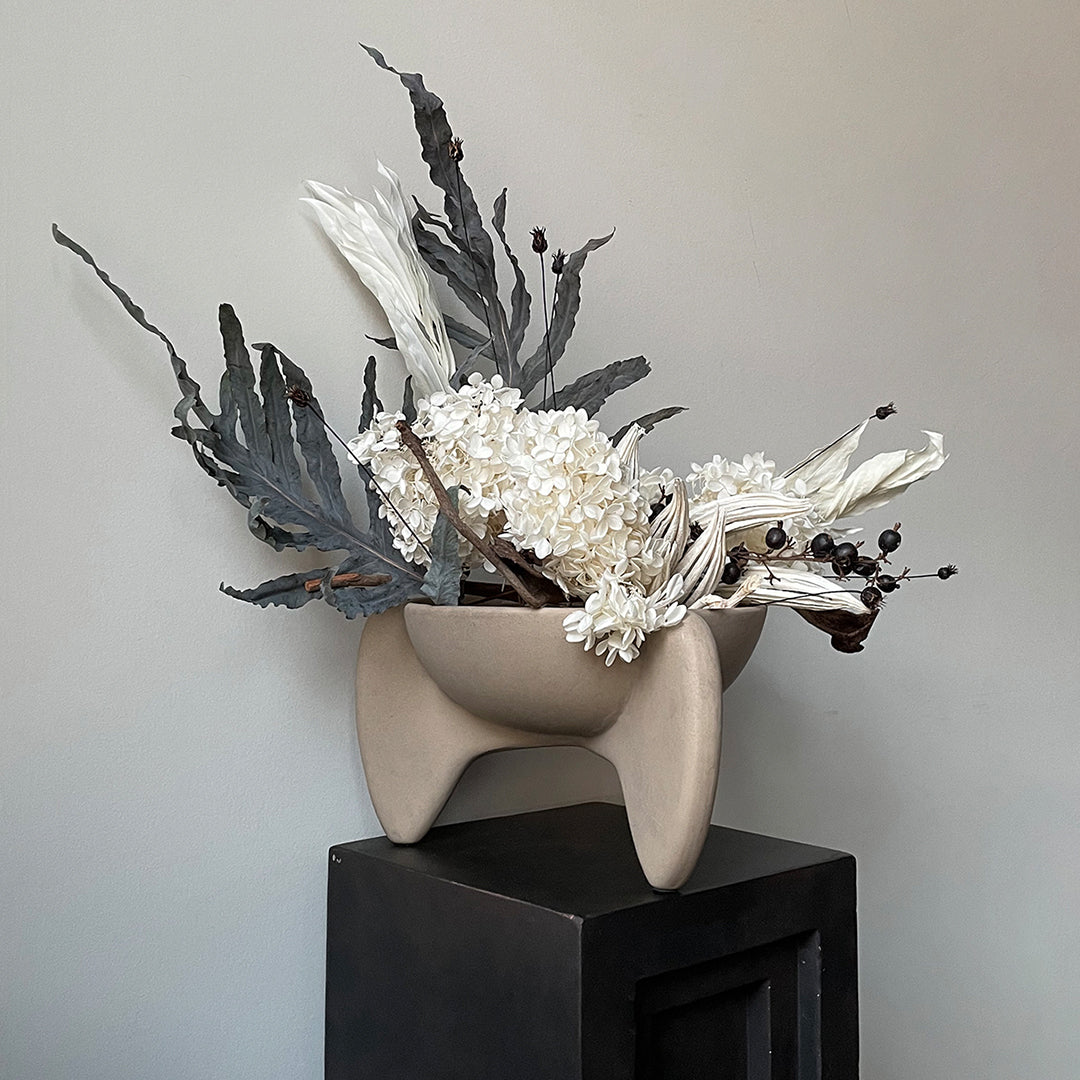 Neutral beige vase with textured white flowers and dark green leaves, adding a modern touch to decor.
