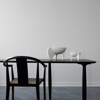 Black chair with a woven seat next to a sleek black table, featuring minimalist white ceramic vases.