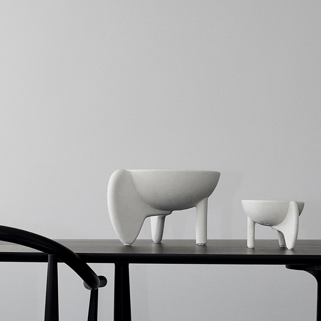Two minimalist white ceramic bowls with unique shapes on a sleek black table against a neutral wall.