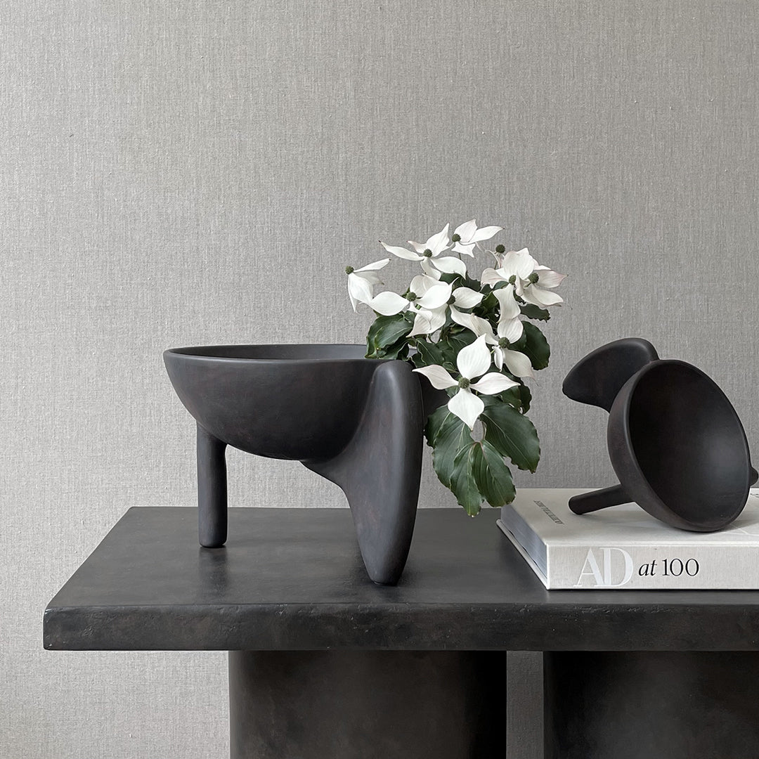 Black minimalist vase with smooth texture, featuring simple shapes and clean lines on a stylish stone surface.