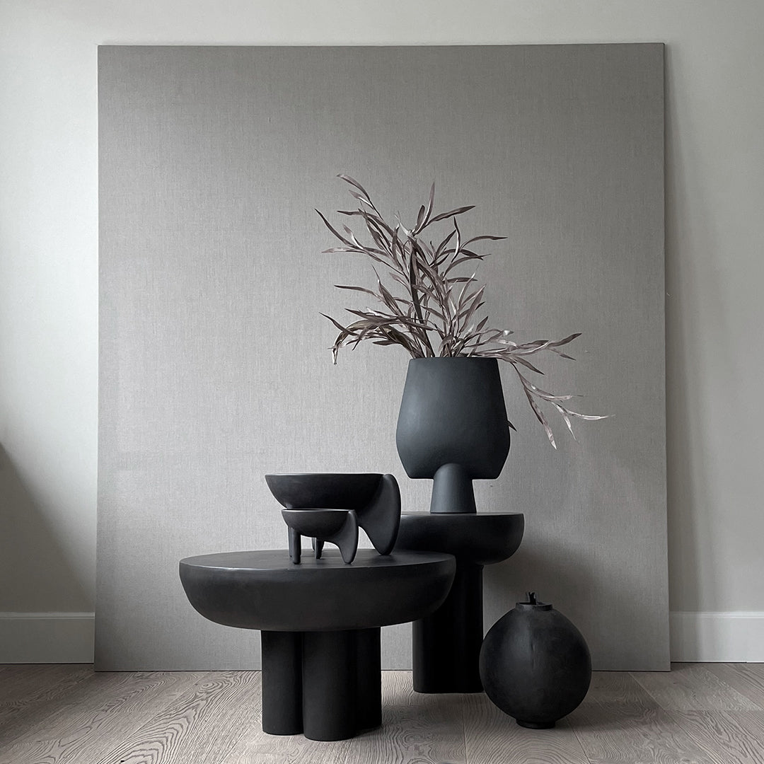 Black ceramic vases and bowls in various shapes against a neutral gray background, featuring modern minimalist design.