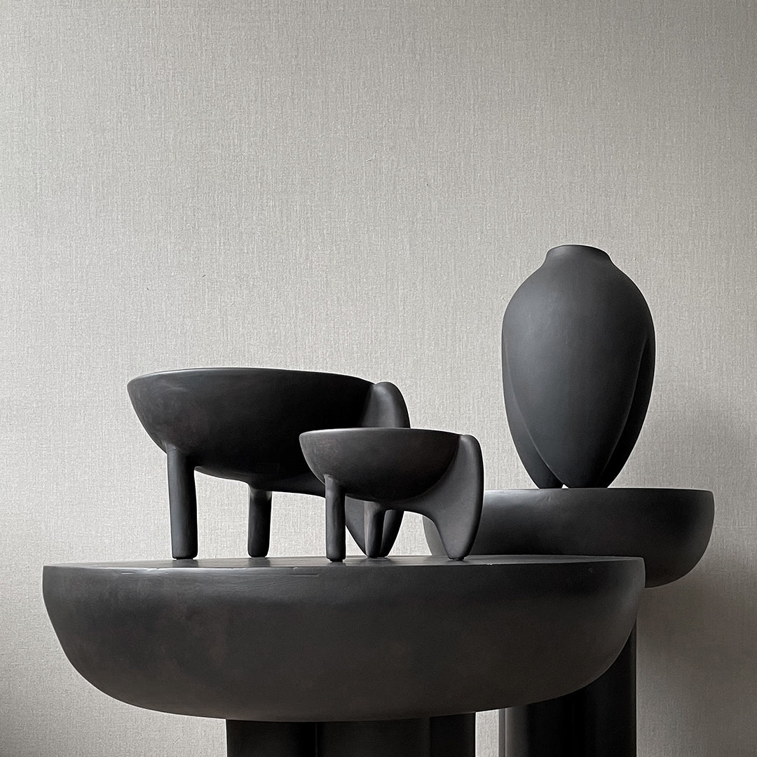 Glossy black ceramic vases with unique shapes and sleek silhouettes, set against a neutral textured background.