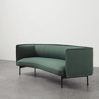 Elegant green upholstered sofa with a sleek curved design and minimalist black legs on a gray floor.