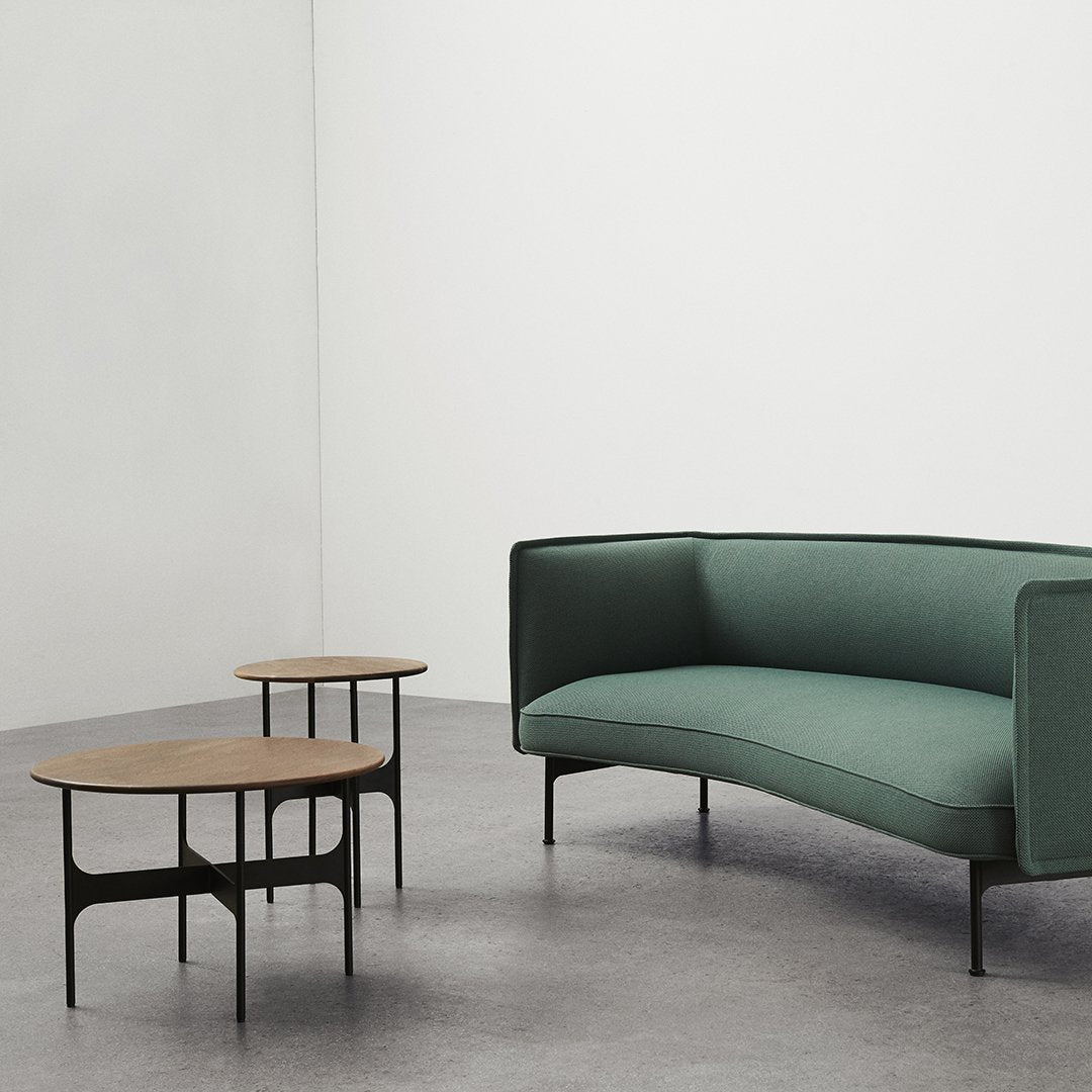 Green curved sofa with black legs and two round, natural wood-topped coffee tables on a light gray floor.