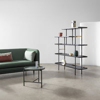 Modern black and gold shelving unit with green sofa featuring soft gray and blush accents on a polished concrete floor.