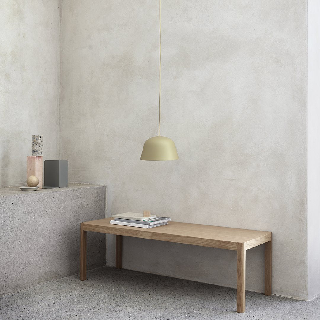 Wooden table with a light brown finish, paired with a soft yellow pendant light against a neutral gray wall.