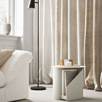 Modern white side table with a sleek design, complemented by neutral beige curtains and light wood flooring.