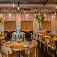 Modern restaurant with warm wooden tones, soft lighting, and green foliage accents. Stylish, inviting, and contemporary decor.