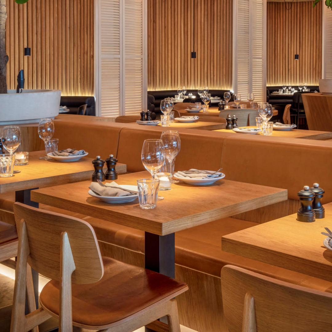 Wooden tables with warm brown tones, paired with clear glassware and sleek black salt and pepper shakers. Modern dining setup.