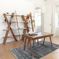 Modern wooden desk and bookshelf in a bright room, with a grey patterned rug on light wooden flooring.