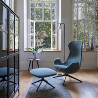 A soft blue armchair with a matching ottoman, set against a warm wood floor and natural light from large windows.