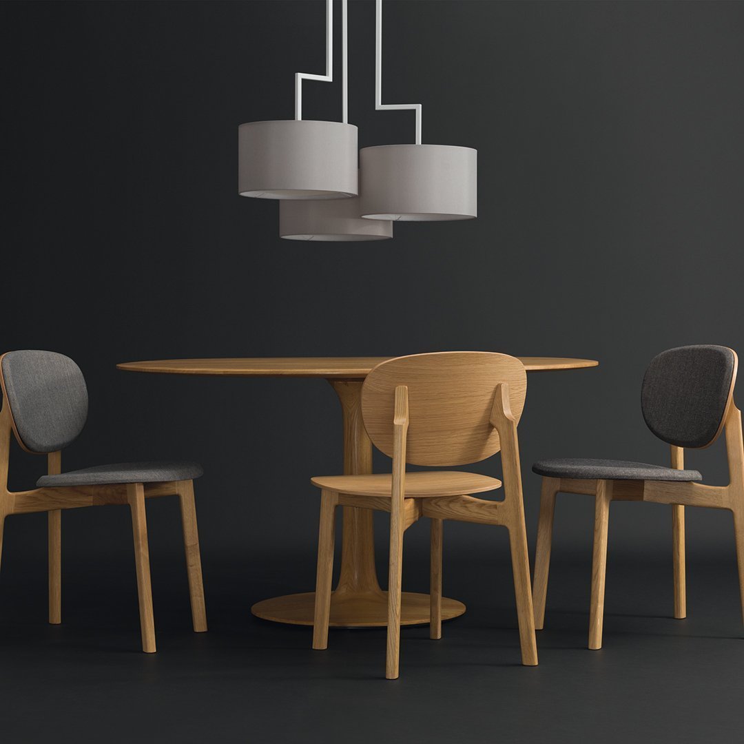 Modern wood dining table with light gray and dark gray upholstered chairs, complemented by gray pendant lamps on a dark backdrop.