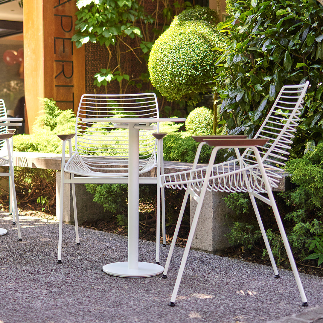 "White striped outdoor chairs and table surrounded by lush green foliage, showcasing modern design and vibrant colors."
