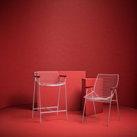 Red backdrop with two white wire chairs featuring horizontal lines and a matching red square table.