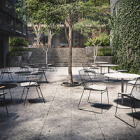 "Modern outdoor café setting with gray stone flooring, black and white chairs, and lush greenery backgrounds."