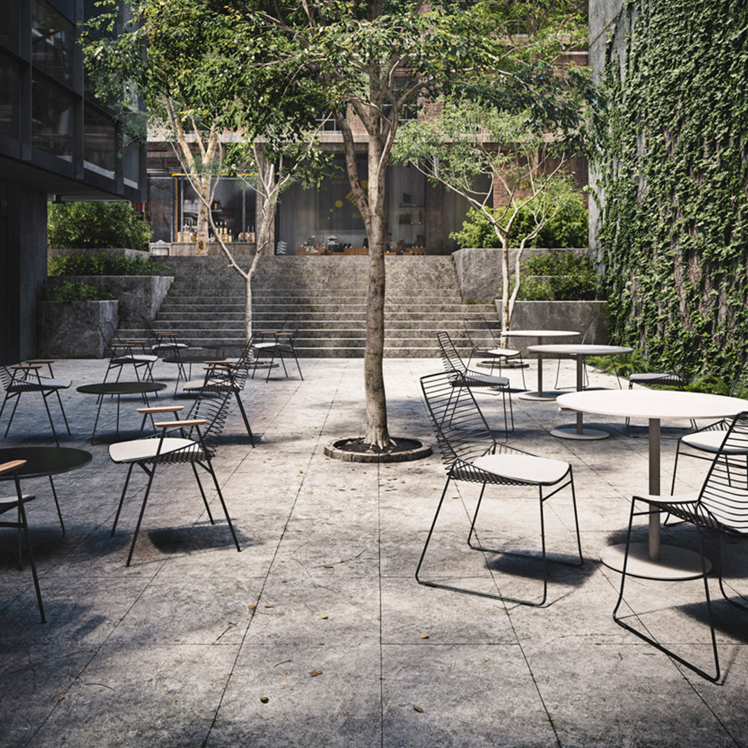 Modern outdoor patio with black and white chairs, concrete flooring, and greenery. Minimalist and stylish design.