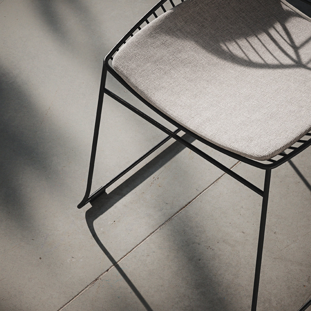 Modern black chair with a light gray fabric seat, featuring sleek lines and minimalist design, set against a neutral floor.