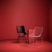 Two modern chairs—one black, one white wire design—set against a vibrant red background.