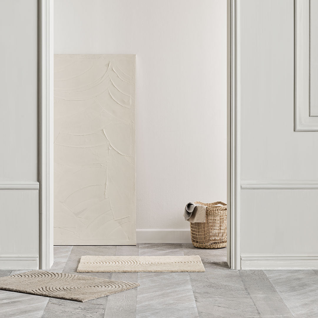 Beige textured wall art with natural woven basket, contrasted by gray and white patterned flooring and light walls.