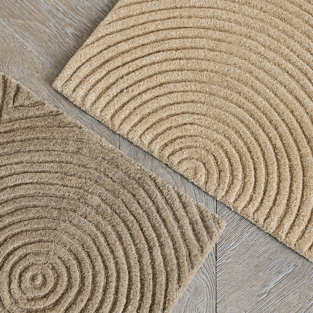 Beige area rugs with textured spiral patterns and soft, circular designs on a light wood floor.