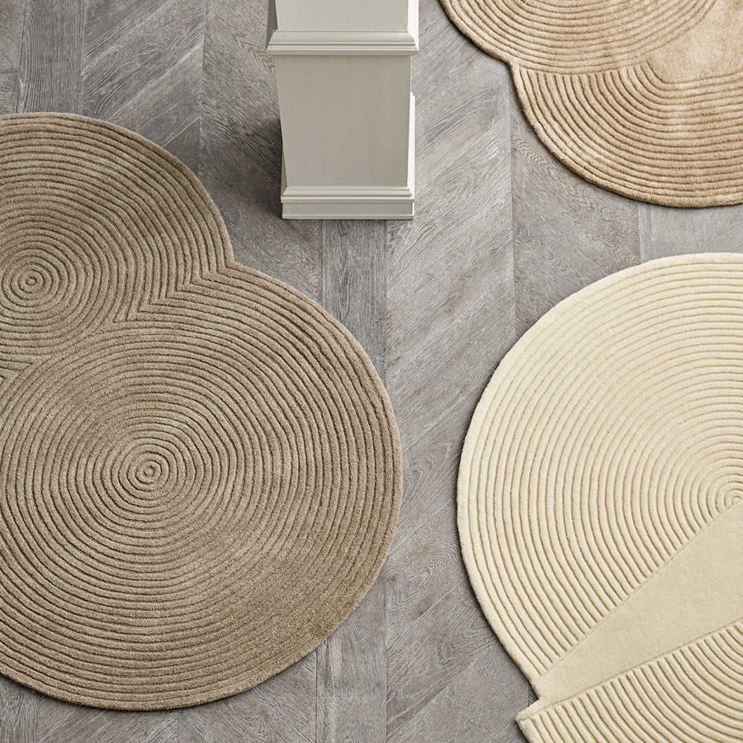 "Beige and cream circular rugs with spiral patterns on a gray wood floor."