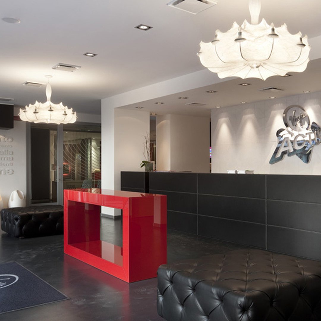 Red reception desk against black and gray walls, with chic white chandeliers and dark leather seating.