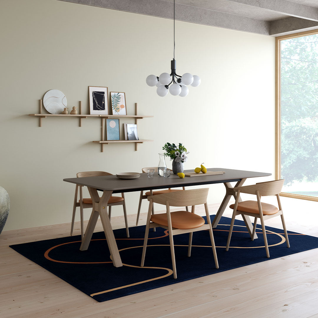 Stylish dining room featuring a navy rug with bold orange patterns, light wood furniture, and soft beige walls.