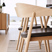 Light wood dining chairs with dark leather seats, featuring a modern design and clean lines in a bright interior setting.