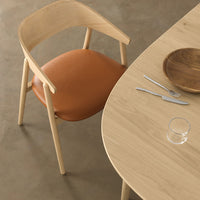 Modern chair with a warm orange cushion and natural wood frame, set against a light wood table.