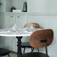 Elegant marble table with sleek black chairs and warm wooden accents against a soft green wall, creating a modern aesthetic.