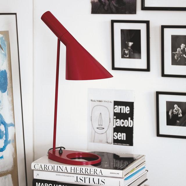 Red angled lamp on stacked books, featuring a sleek modern design against a gallery wall.