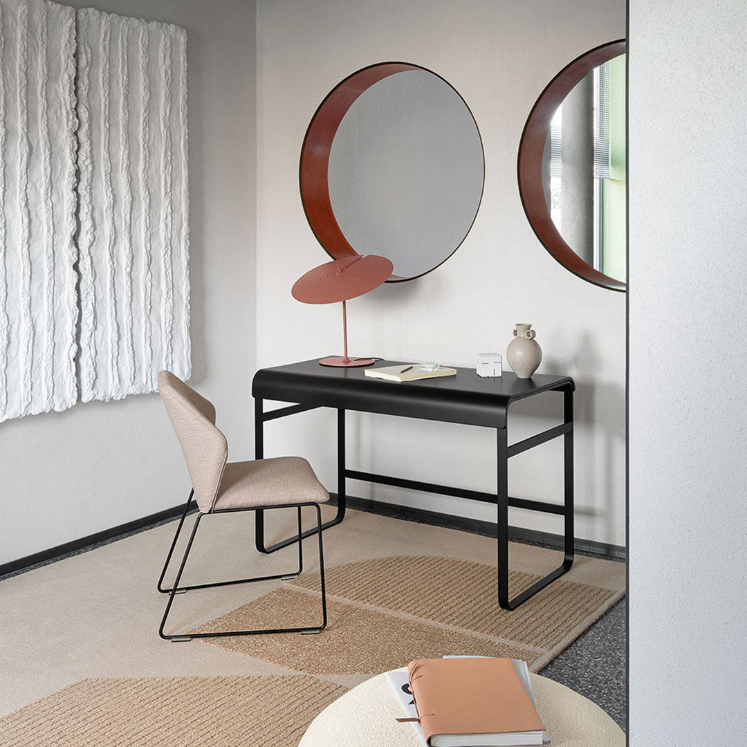 Minimalist workspace featuring soft beige chair, sleek black desk, and round mirrors with warm brown frames.