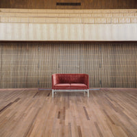 Red upholstered sofa with a sleek silver base, set against a wooden backdrop and flooring.