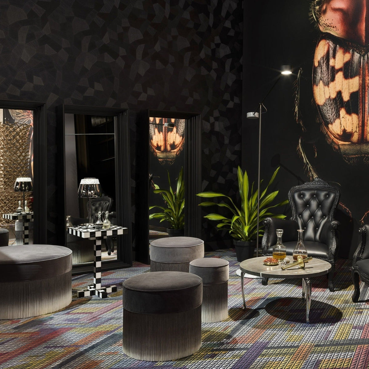 Plush gray ottomans on a vibrant multi-colored patterned rug, with sleek black walls and contrasting decor elements.