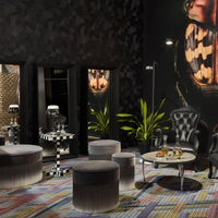 Plush gray ottomans on a vibrant multi-colored patterned rug, with sleek black walls and contrasting decor elements.