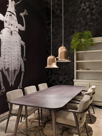 Elegant dining room featuring a dark patterned wall, soft beige chairs, and copper pendant lights, creating a modern ambiance.