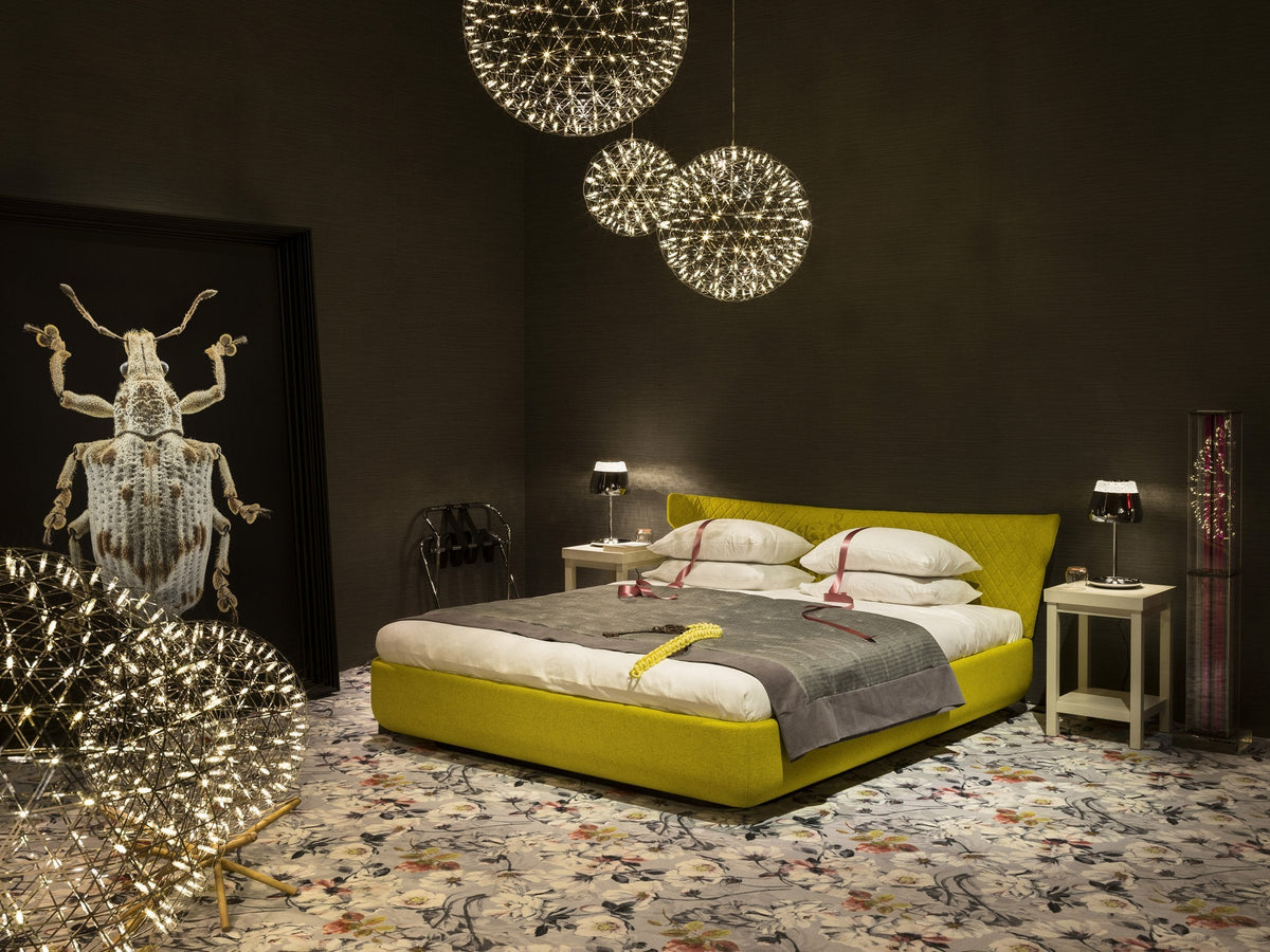 Modern bedroom featuring a vibrant yellow bed, grey throw, and colorful floral patterned rug against a dark wall.
