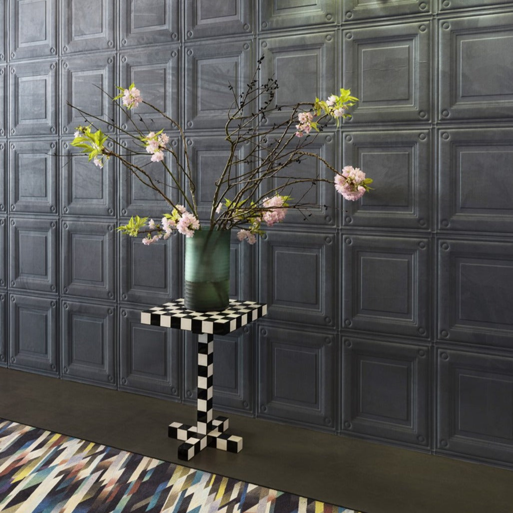 "Vibrant floral arrangement in a glass vase atop a black and white checkered table, against a textured gray wall."