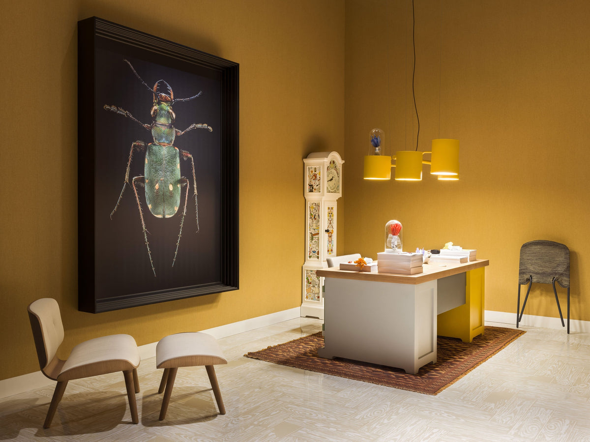 Modern workspace featuring yellow accents, earthy tones, and a striking black insect art piece on a textured wall.