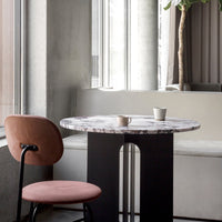 Round marble table with gray and white veining, paired with a blush pink chair against a minimalist backdrop.